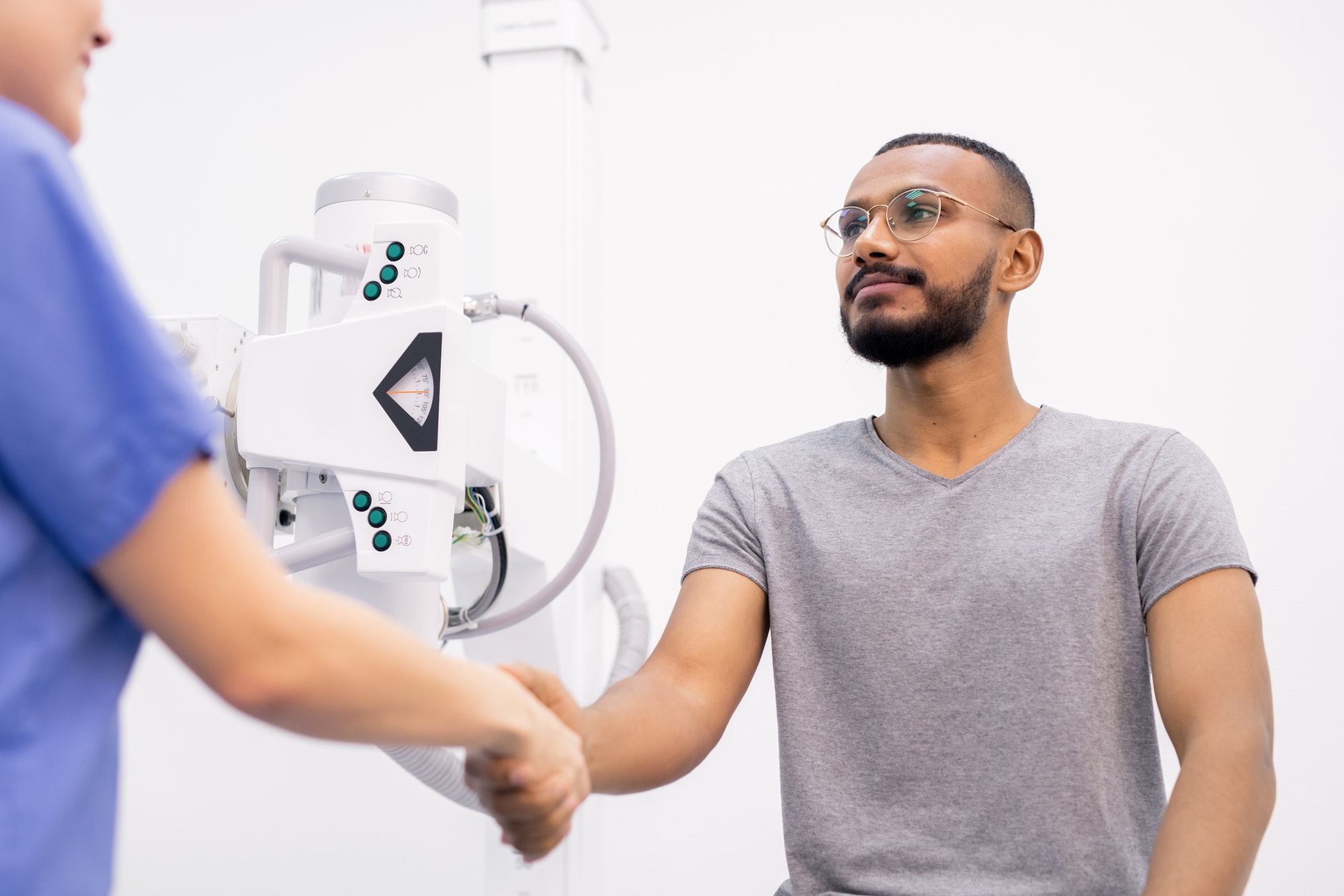Young grateful intercultural patient shaking hand of his doctor after recovery